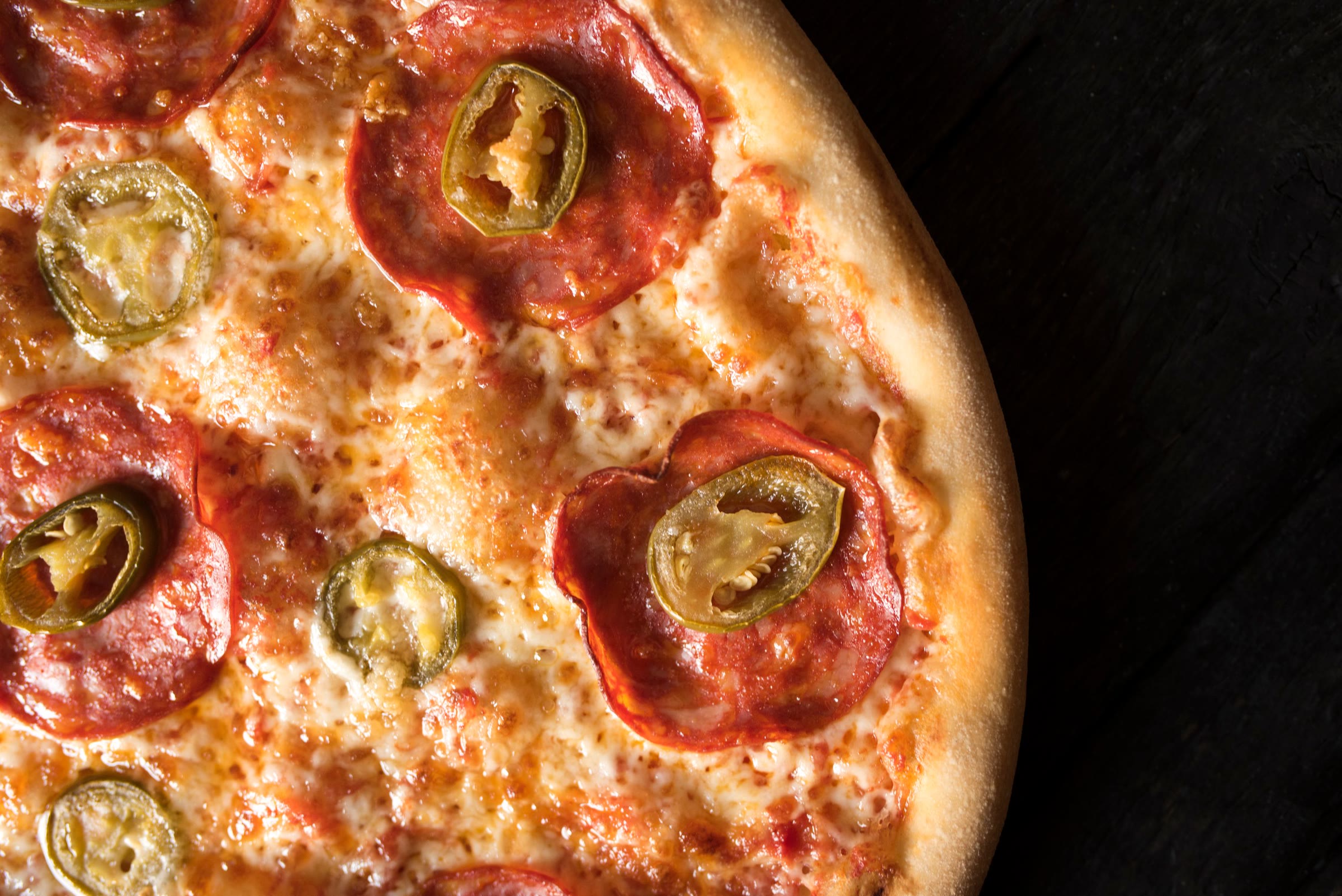 A baked pizza topped with spicy cured sausage and sliced jalapeños