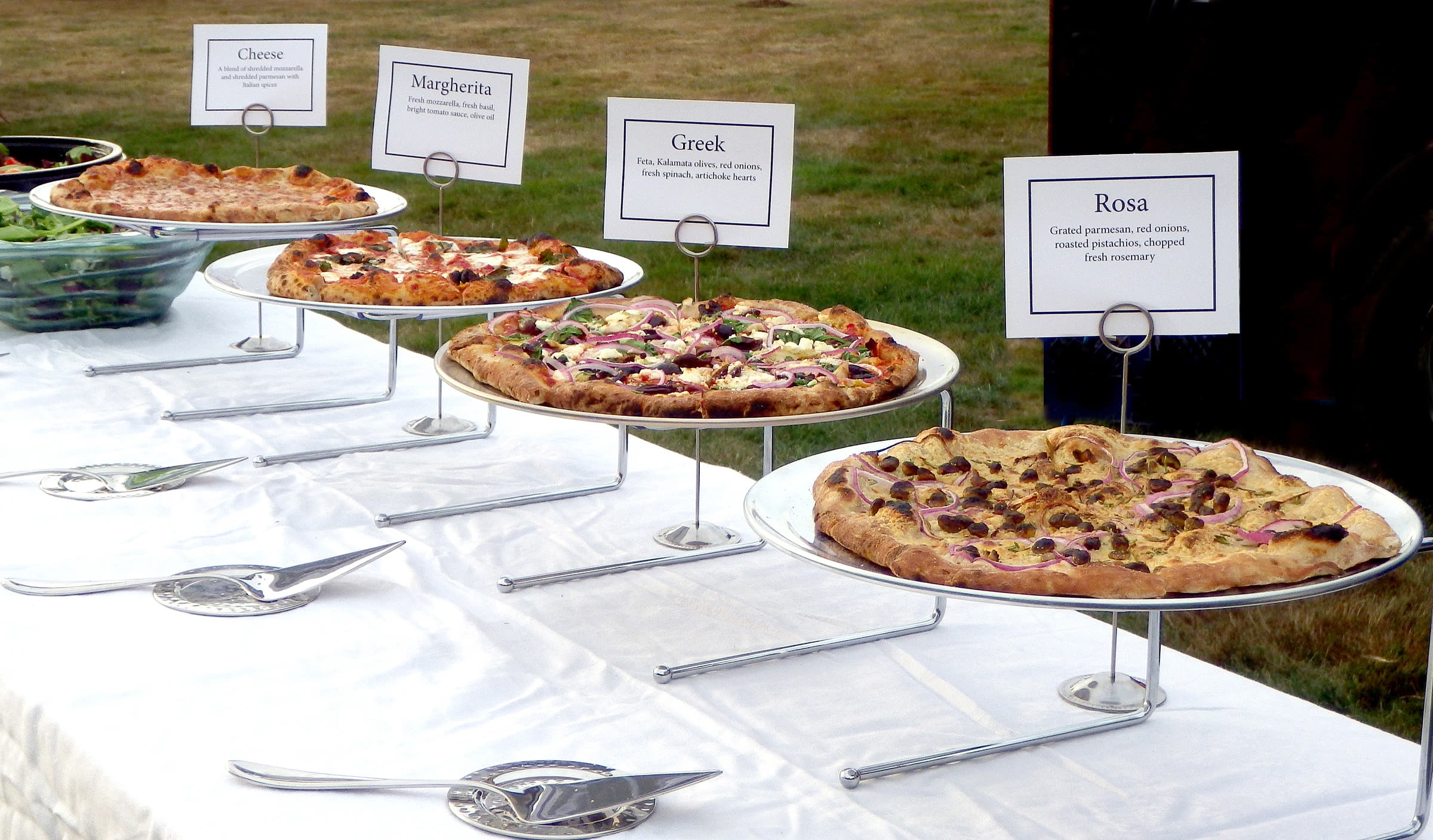 A wedding buffet of wood-fired pizzas on stands with hand-lettered name cards