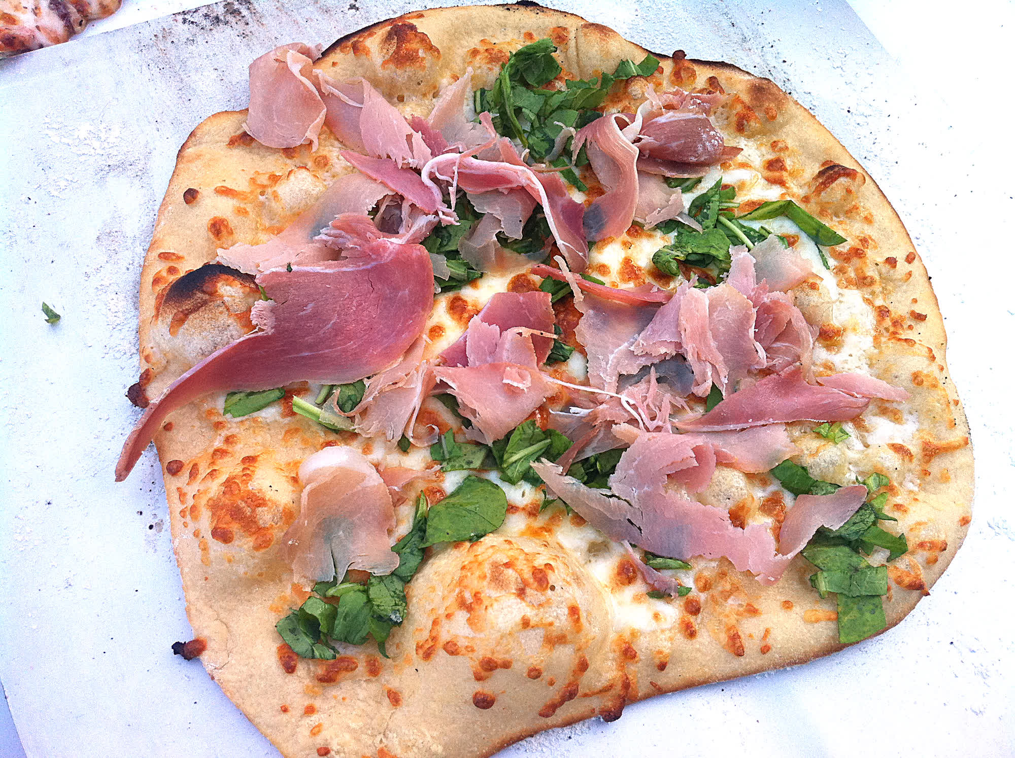 A thin-crust pizza topped with prosciutto and fresh greens