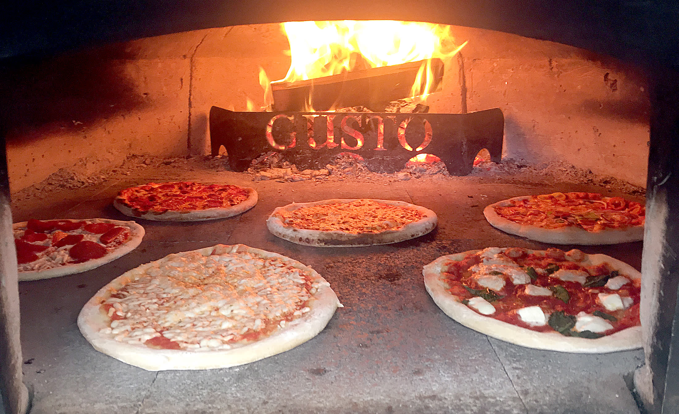 Six pizzas baking around the fire inside the branded Gusto oven