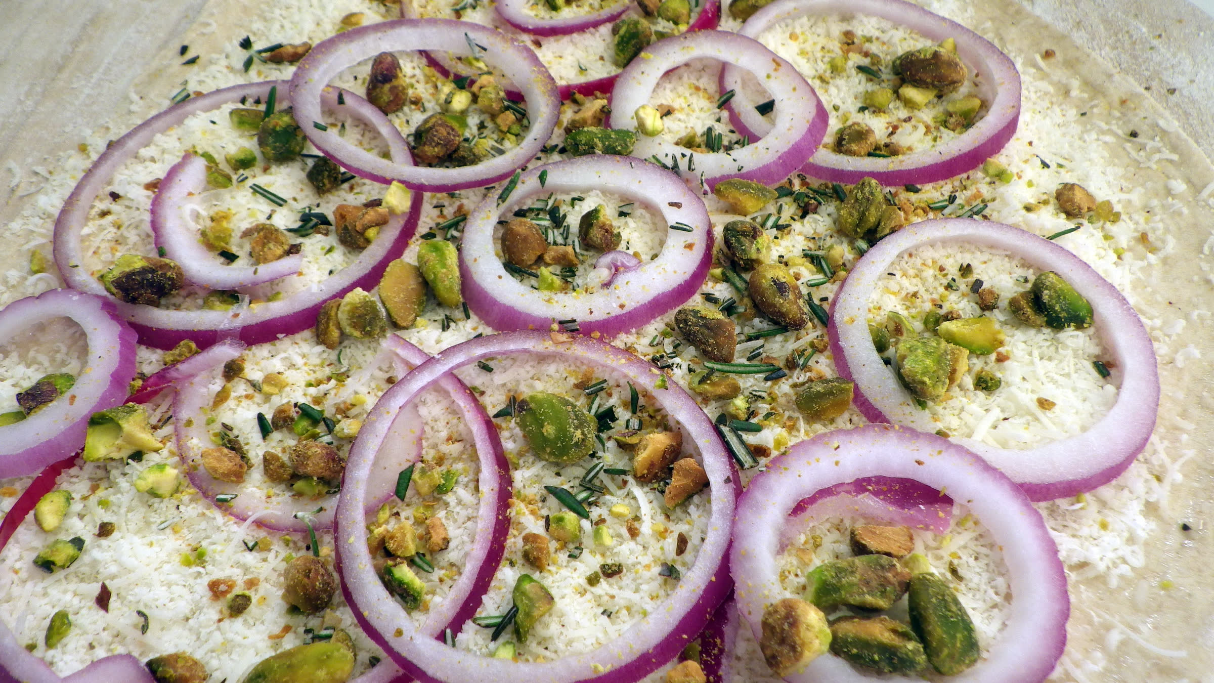A white Rosa pizza with red onion, roasted pistachios, and rosemary